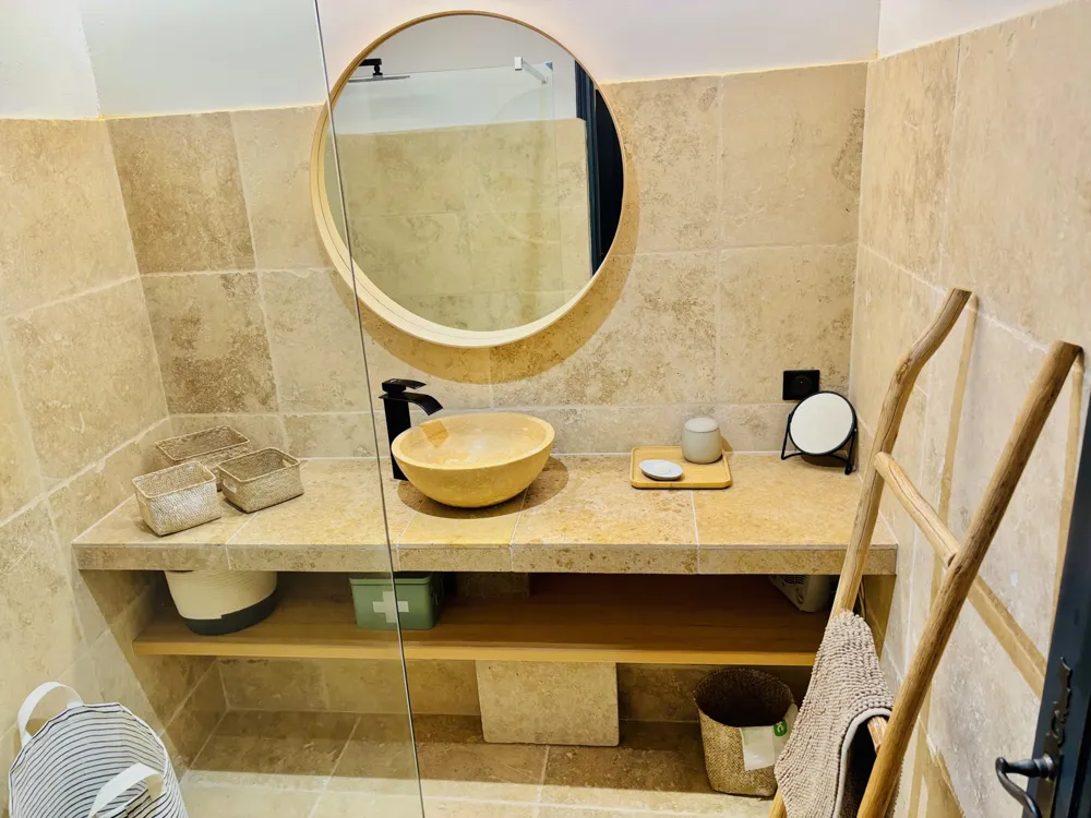 Light stone bathroom with round mirror and basin