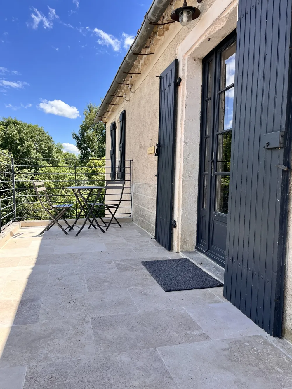 Stone-paved terrace in front of French windows with black shutters